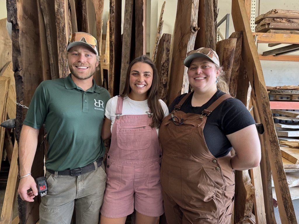 Cole and Sarah Miller with a member of the Revolve Reclaimed crew, standing in front of racks of live-edge slabs in the Denver yard