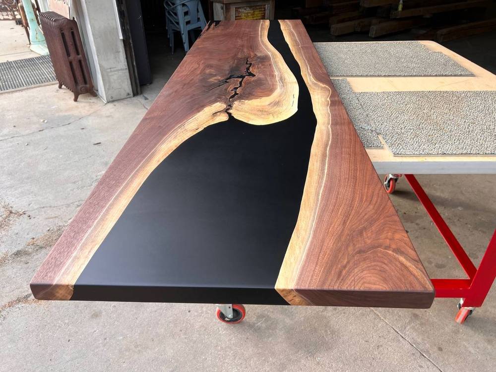 Black walnut live edge dining table with black epoxy fill, viewed at an angle in a bright room